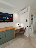 Una habitación moderna con un escritorio de madera, una silla, un televisor de pantalla plana en la pared y un equipo de aire acondicionado integrado.