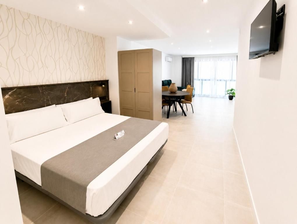 Una habitación de hotel moderna con una cama grande, una zona de comedor y un televisor montado en la pared.