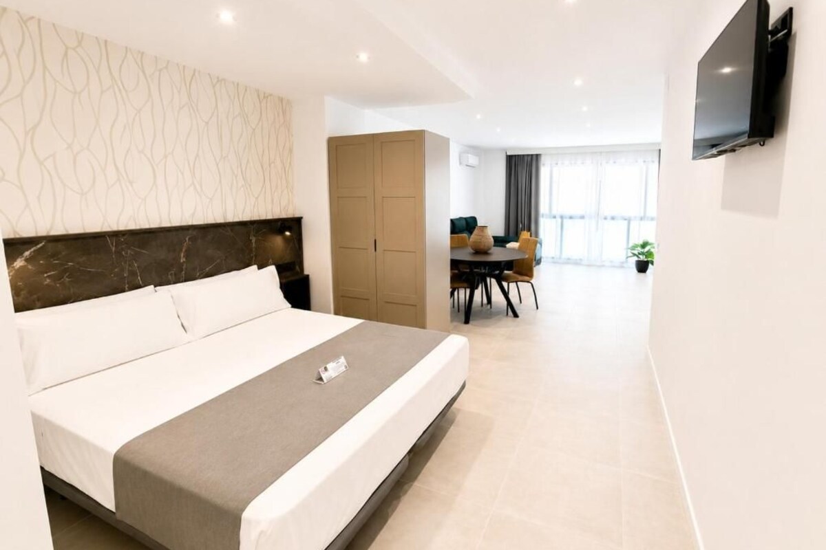Una camera d'albergo moderna con un letto grande, un'area pranzo e una TV a parete.