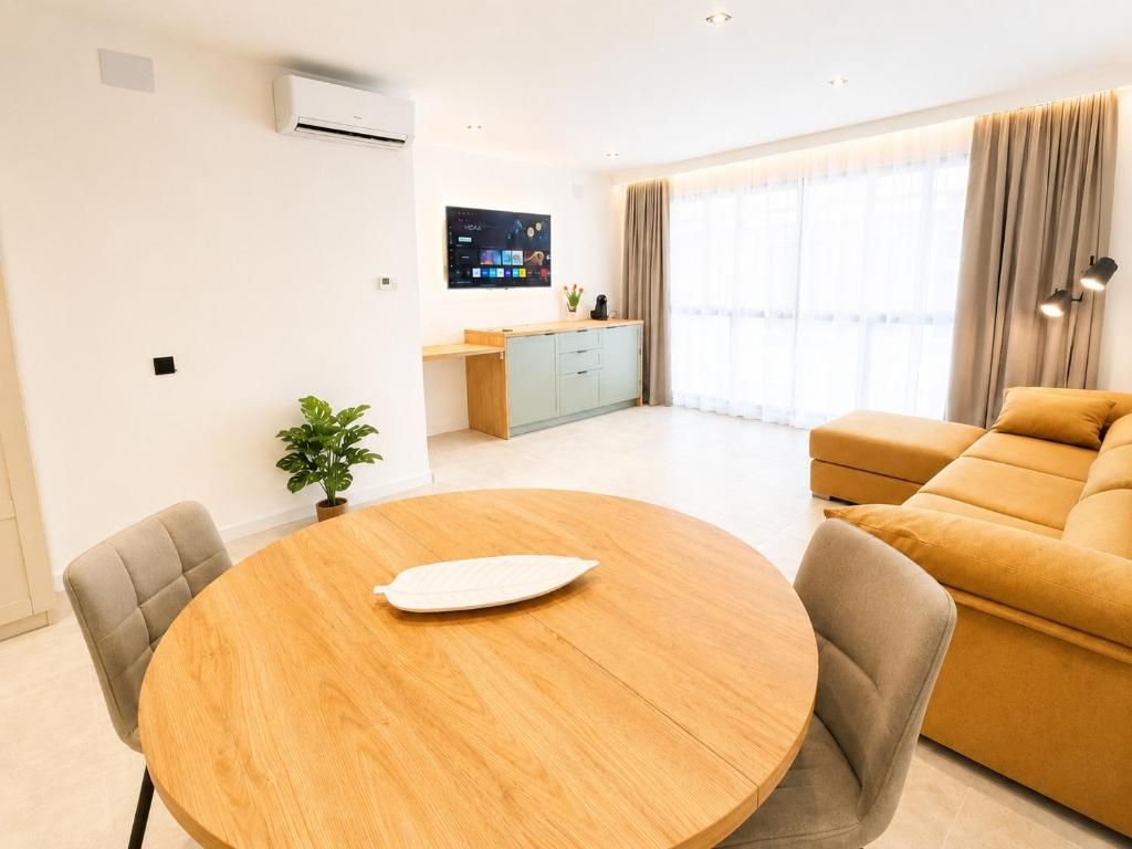 Una sala de estar moderna con una mesa redonda de madera, un sofá y un televisor montado en la pared.