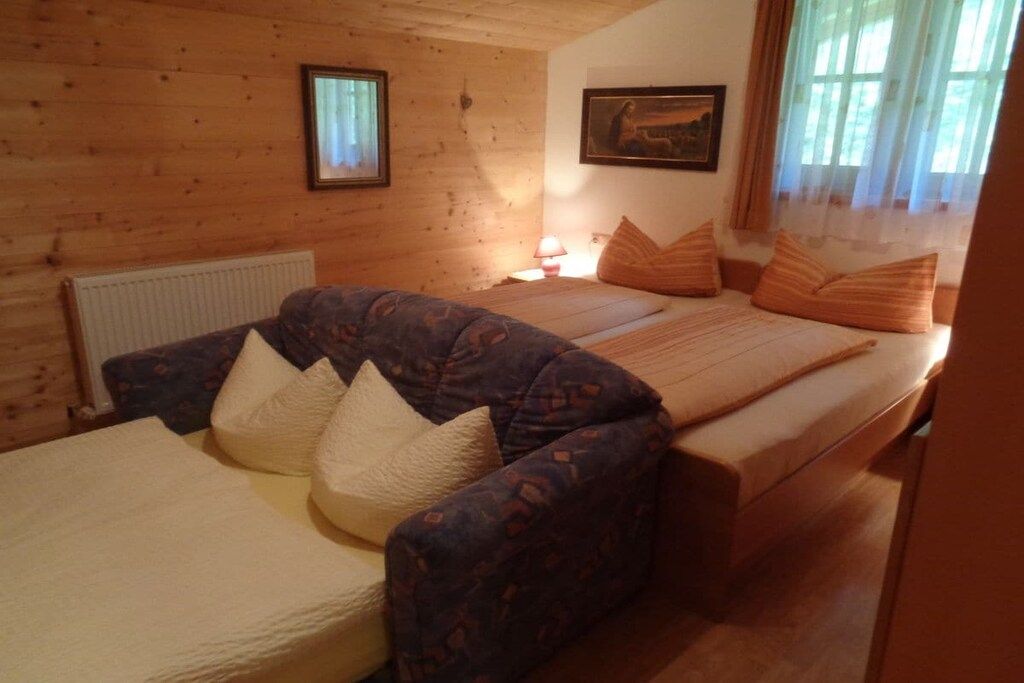 A room with a sofa, a bed, a radiator, and a window with curtains.