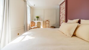 Een goed verlichte slaapkamer met een groot bed, een stoel, een klein tafeltje en een decoratief wandpaneel.