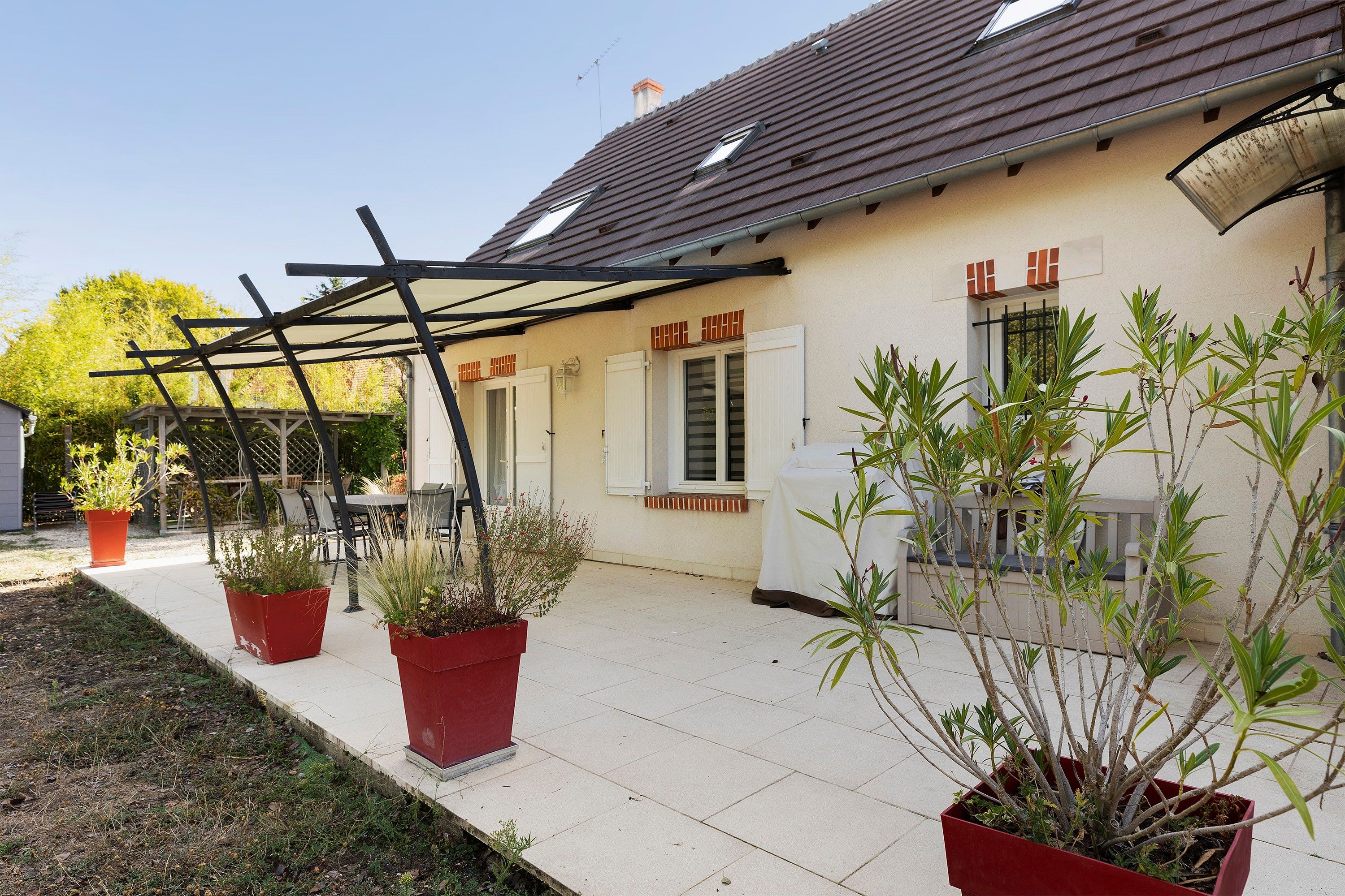 A residential building with a covered patio area, potted plants, and a clear sky.
