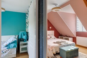 A bedroom with a sloped ceiling, a bed with a blue cover, a nightstand, and a dresser.
