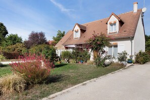 A two-story house with a sloped roof, a front porch, and a garden with various plants and flowers. - Bed and Breakfast 'Étap' Châteaux - Chambre Familiale' with Shared Terrace, Shared Garden and Wi-Fi (Cheverny)