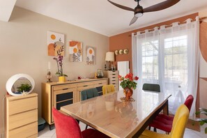 A dining area with a wooden table, chairs, a ceiling fan, and artwork on the walls.