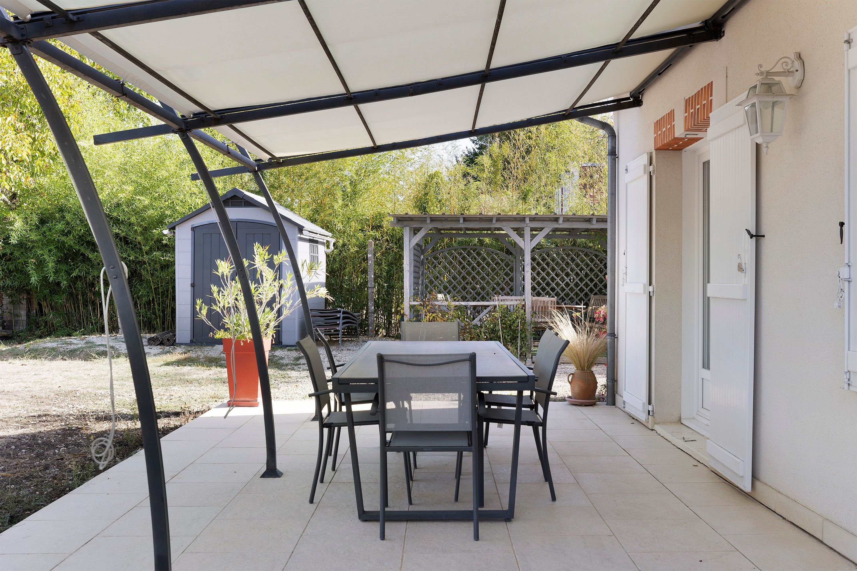 Un patio al aire libre con una mesa y sillas, una zona cubierta y un cobertizo al fondo.