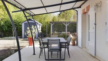 Un patio al aire libre con una mesa y sillas, una zona cubierta y un cobertizo al fondo.