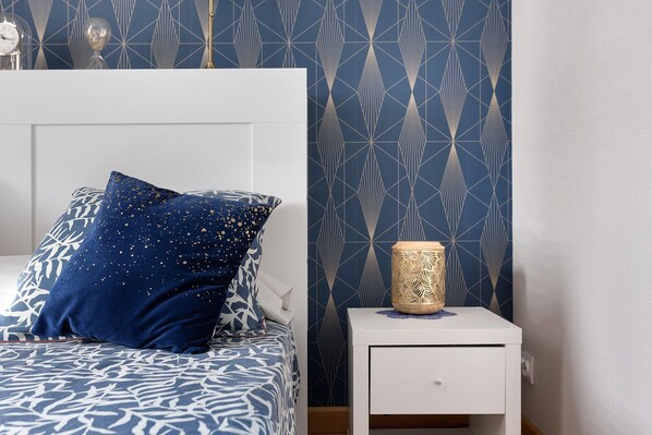 A bedroom with a bed, a nightstand, a decorative vase, and a wall with a geometric pattern.