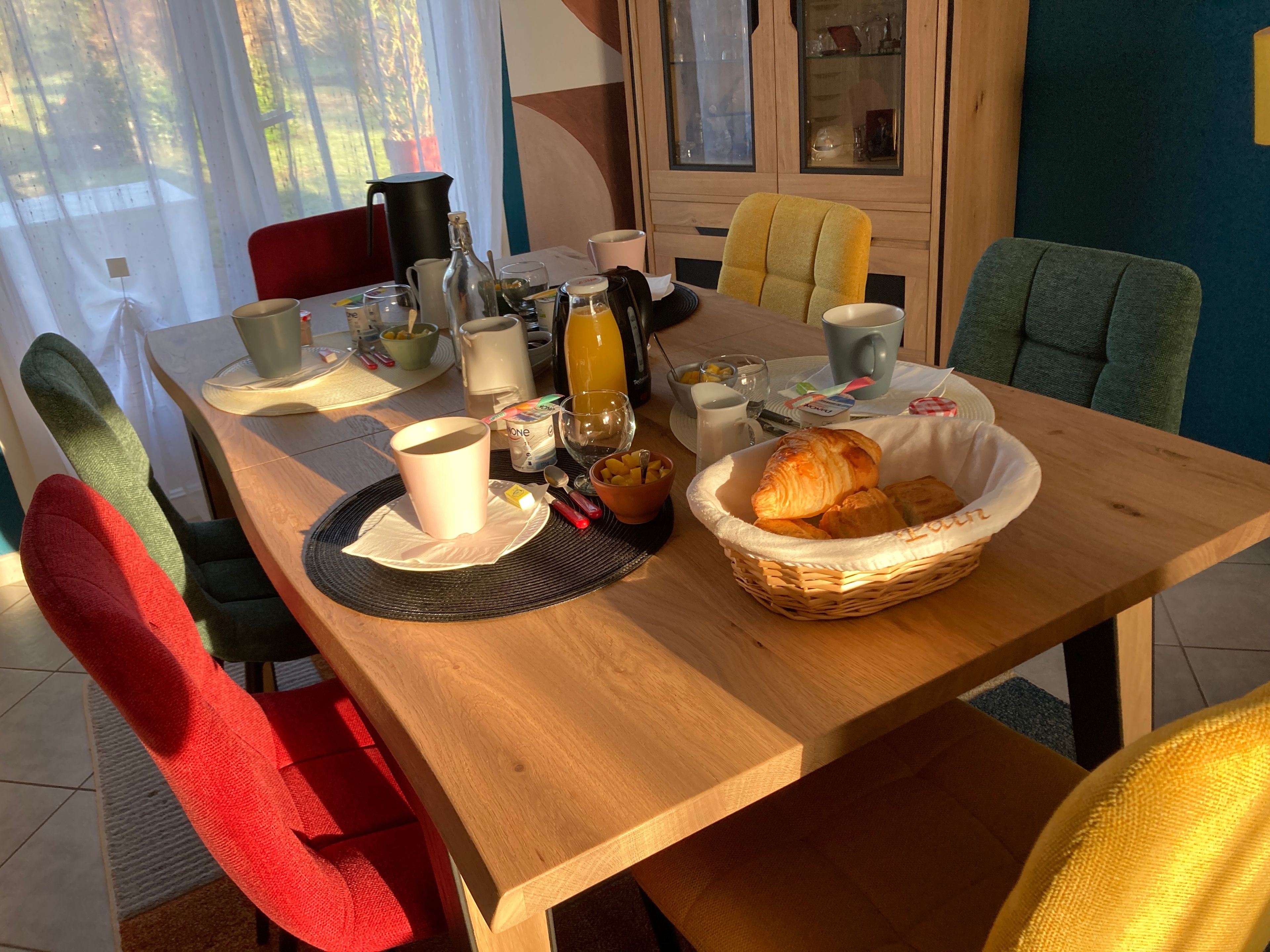 Uma mesa de café da manhã com um cesto de croissants, uma xícara de café e diversos itens para o café da manhã.