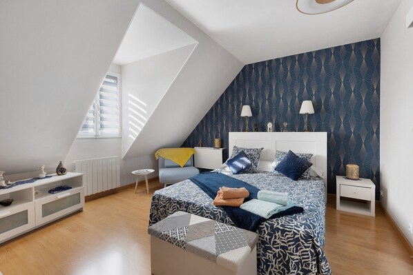 A bedroom with a sloped ceiling, a bed with patterned bedding, a nightstand, a bedside lamp, and a window with blinds.