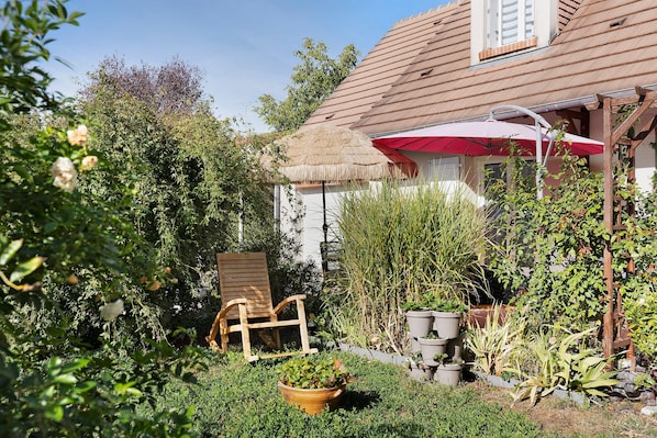 A garden with a wooden chair, potted plants, and a thatched roof structure.