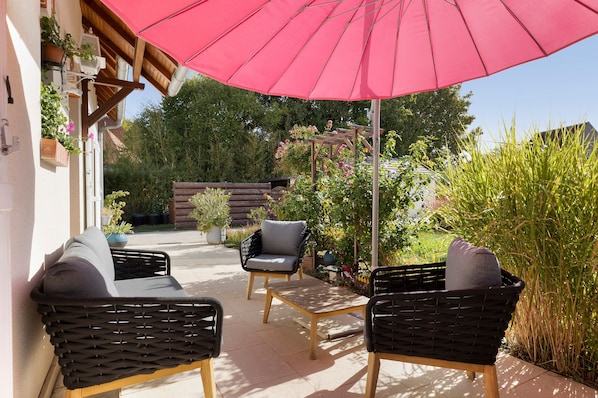An outdoor patio area with wicker furniture, a wooden table, and a red umbrella.