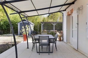 An outdoor patio with a table and chairs, a covered area, and a shed in the background.