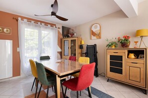A dining area with a wooden table, colorful chairs, a ceiling fan, and a cabinet with decorative items.