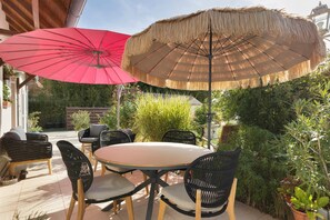 An outdoor patio with a round table and four chairs, two large umbrellas, and lush greenery.
