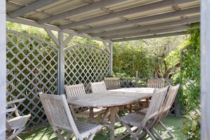 A covered outdoor seating area with a table and chairs, surrounded by a lattice fence and greenery.