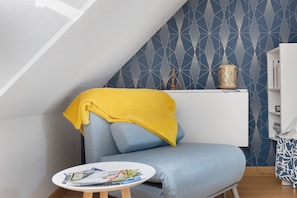 A corner of a room with a blue patterned wall, a white bookshelf, and a small round table with magazines.