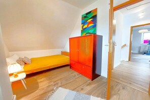 A small bedroom with a single bed, a red wardrobe, and a colorful abstract painting on the wall. - Holiday home in Lindau with swimming pool (Lindau)