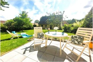 An outdoor patio with a round table and four chairs, surrounded by a well-maintained lawn and a house in the background. - Holiday home in Lindau with swimming pool (Lindau)