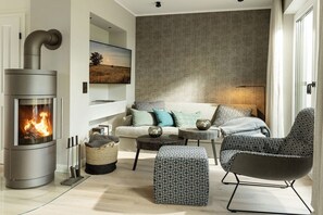 Ein modernes Wohnzimmer mit eingebautem Holzofen, einer Couch, einem gemusterten Hocker und einem Sessel.