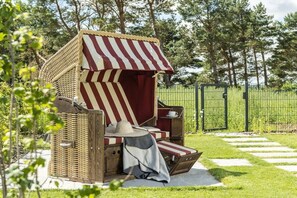 Eine Sitzgruppe im Freien aus Rattangeflecht mit einem Streifenmarkisenvorzelt, einem Hut und einer Decke.