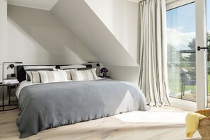 Ein Schlafzimmer mit einem Bett, einem Nachttisch, einer Lampe und Blick durch ein großes Fenster.