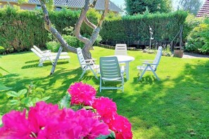 A well-maintained garden with a round table and chairs, surrounded by lush greenery and flowering plants. - Holiday home in Schlei with 2 bedrooms (Brodersby-Burg)