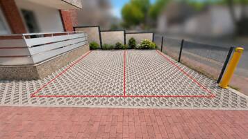 A paved area with a geometric pattern, bordered by a fence and a building with a modern design.