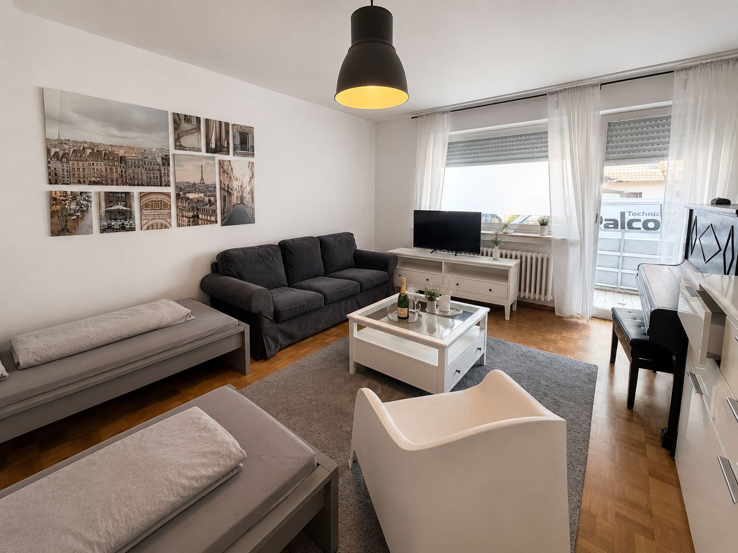 Ein modernes Wohnzimmer mit einer Couch, einem Couchtisch mit einer Flasche, einem Fernseher auf einem Schrank und einem Fenster mit Vorhängen.