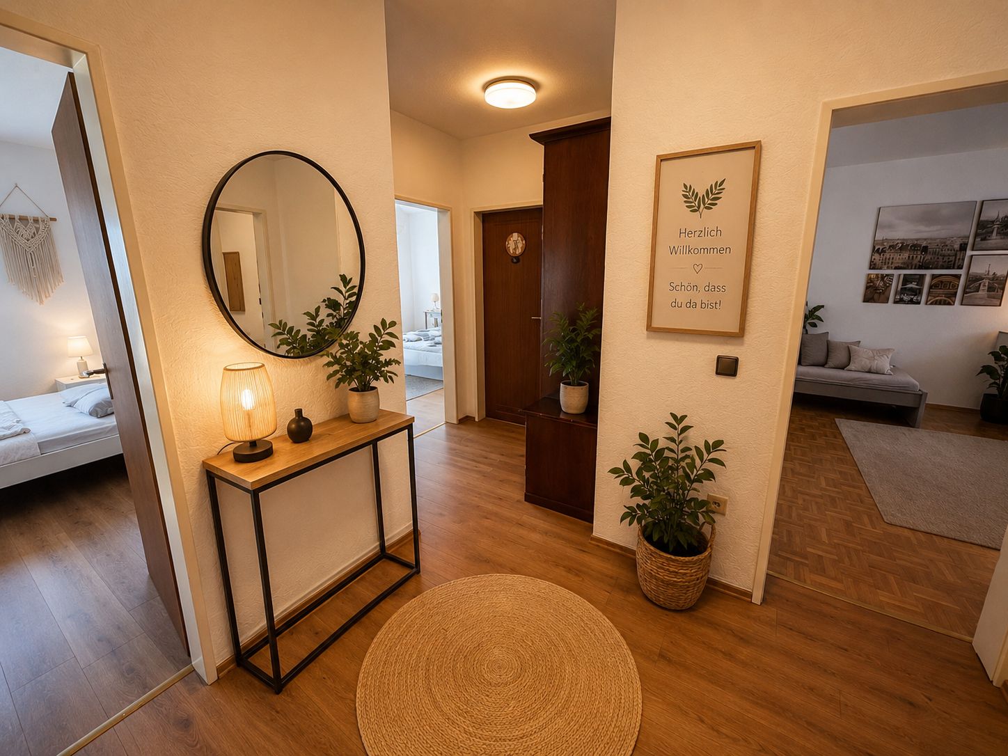 Zona de recepción de hotel con una consola de madera, un espejo redondo, un cartel de bienvenida y vistas a un dormitorio.