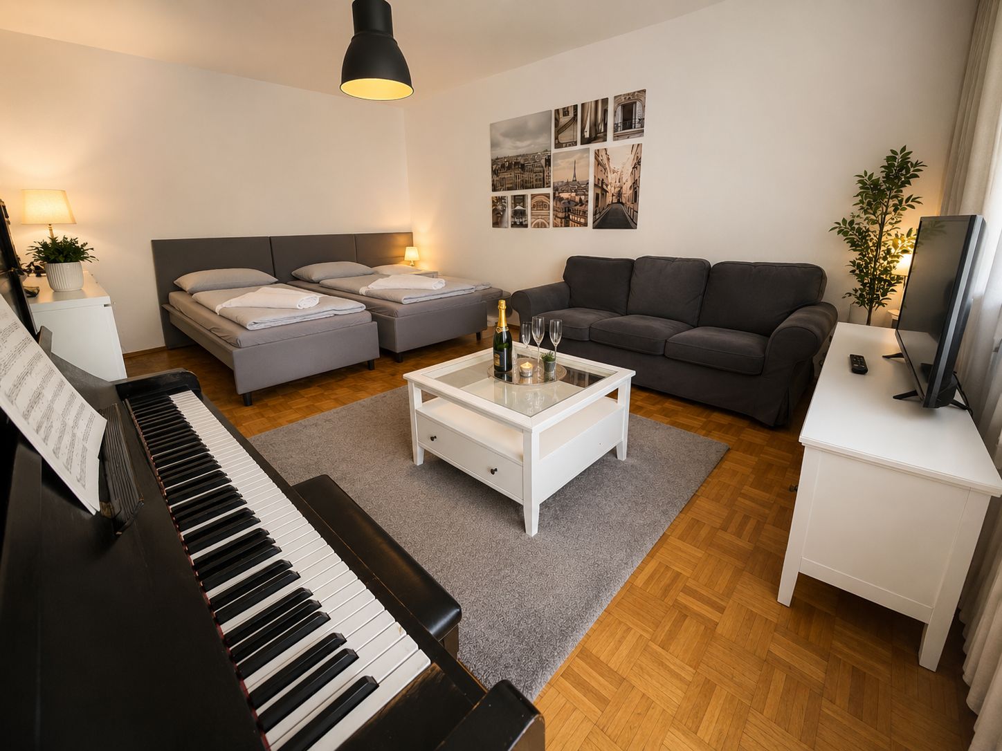 Ein Wohnzimmer mit einem Klavier, zwei grauen Sofas, einem weißen Couchtisch und einem Fernseher auf einem weißen Schrank.