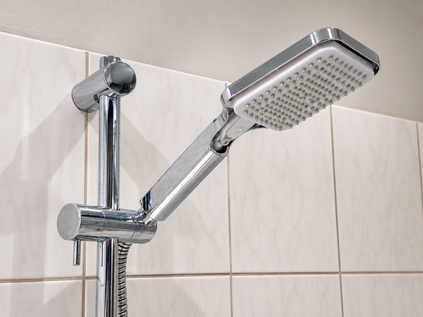 Ein chromfarbener Duschkopf mit Handbrause, an einer Wand mit weißen Fliesen befestigt.