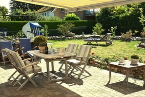 An outdoor patio with a wooden table and chairs, a lawn chair, and a small table with a potted plant. - Holiday home with 2 bedrooms (Heiligenhafen)
