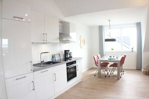 A modern kitchen with white cabinetry, a built-in oven, and a dining area with a table and chairs. - A haven of peace in the sunny garden in Kellenhusen (Kellenhusen)