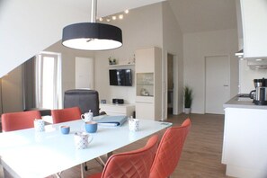 A modern dining area with a white table, red chairs, and a black pendant light. - A haven of peace in the sunny garden in Kellenhusen (Kellenhusen)