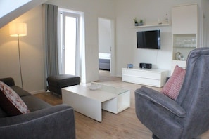 A modern living room with a sofa, armchair, coffee table, and a flat-screen TV mounted on the wall. - A haven of peace in the sunny garden in Kellenhusen (Kellenhusen)