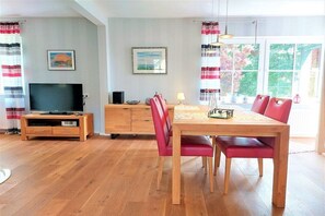 A dining area with a wooden table and red chairs, a television on a wooden stand, and a window with curtains. - Holiday home in Kappeln with swimming pool (Kappeln)