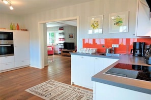 A modern kitchen with white cabinetry, a central island, and a red backsplash. - Holiday home in Kappeln with swimming pool (Kappeln)