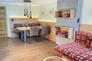 Ein gemütlicher Essbereich mit einem Holztisch, Stühlen und einer Bank. An der Wand befinden sich Regale mit dekorativen Gegenständen und ein rot kariertes Sofa.