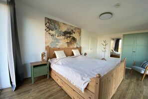 A bedroom with a wooden bed, a nightstand, a green cabinet, a window with a view, and a wall with a textured mural. - Holiday home in Pruchten with swimming pool (Pruchten)