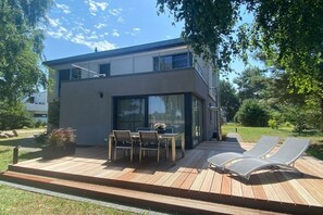 Ein modernes, zweistöckiges Haus mit Terrasse, Sitzgelegenheiten im Freien und einer Glastür.