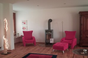 A living room with a fireplace, two pink chairs, a small ottoman, and a glass coffee table. - Holiday home with 2 bedrooms (St. Michaelisdonn)