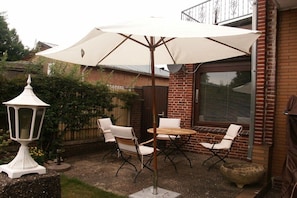 An outdoor patio with a round table and four chairs, a large umbrella, and a white lantern. - Holiday home with 2 bedrooms (St. Michaelisdonn)
