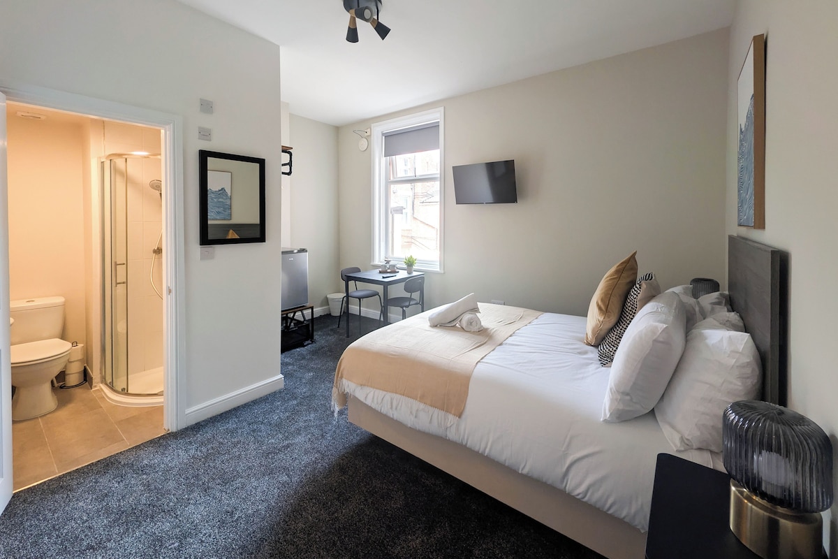 Ett hotellrum med en säng, ett skrivbord, en tv och en dusch.