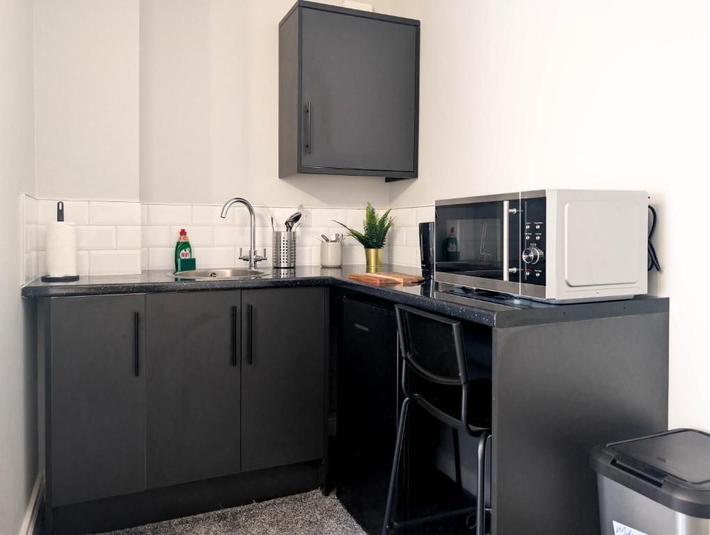 A compact kitchen with dark cabinets, a microwave, a sink, and a small trash bin.