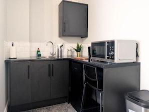 Cocina compacta con armarios oscuros, microondas, pileta y un pequeño bote de basura.