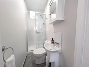 Un baño con cabina de ducha de vidrio, inodoro blanco y lavabo con espejo superior.