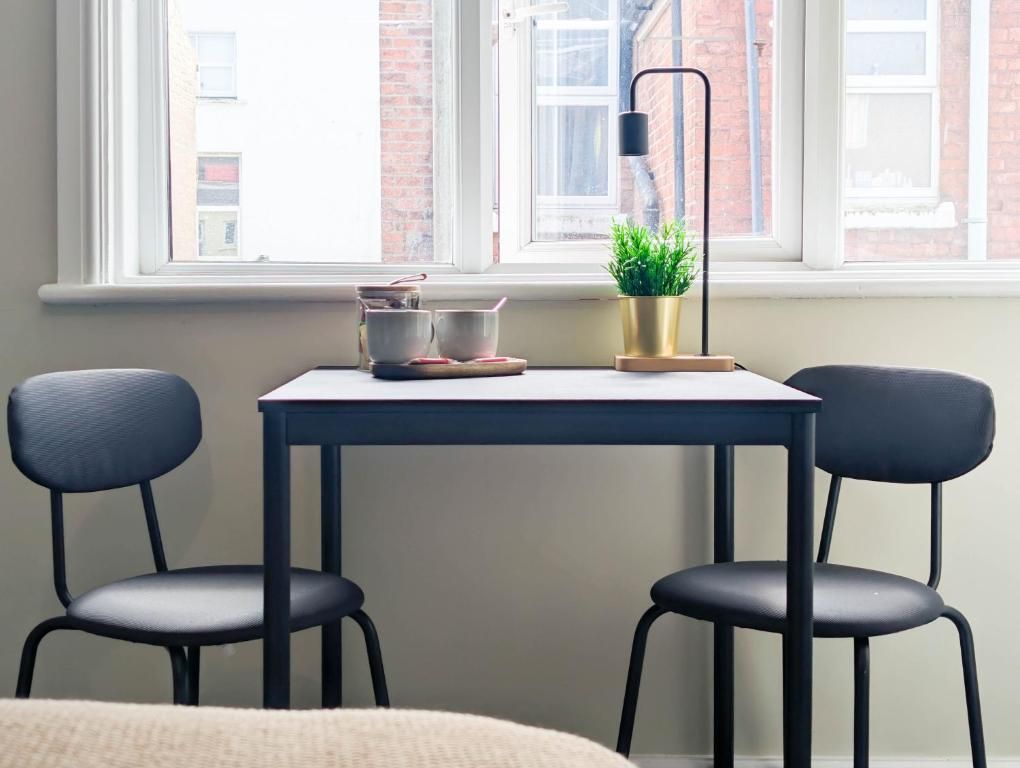 A room with a table and two chairs, a potted plant, a lamp, and a window with a view of buildings.