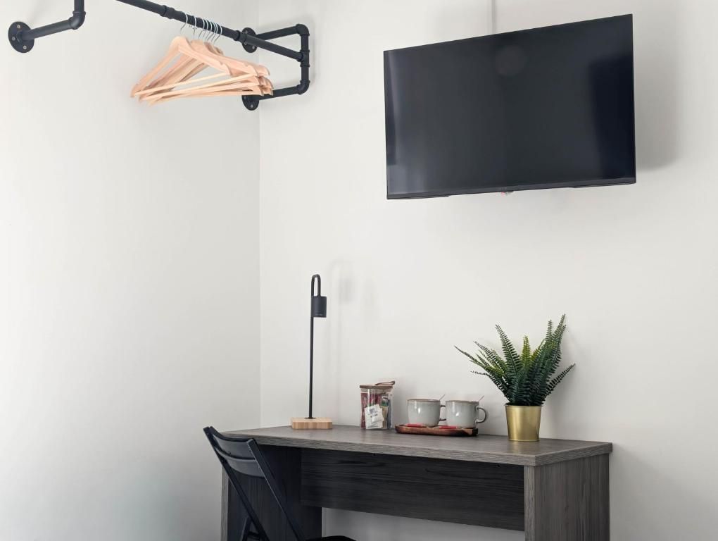 A modern room with a desk, a flat-screen TV mounted on the wall, a hanging light fixture, and a potted plant.
